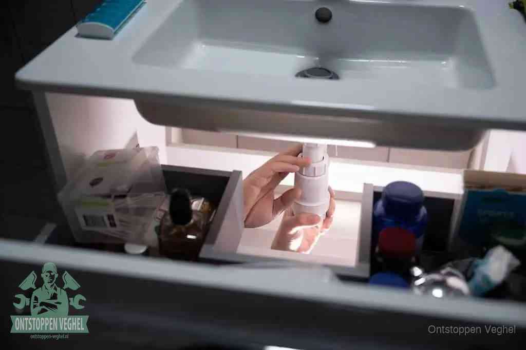 Een pompfles met zeep boven een wastafel, de heet water en afwasmiddel-methode om een vetprop in de afvoer los te maken in Veghel