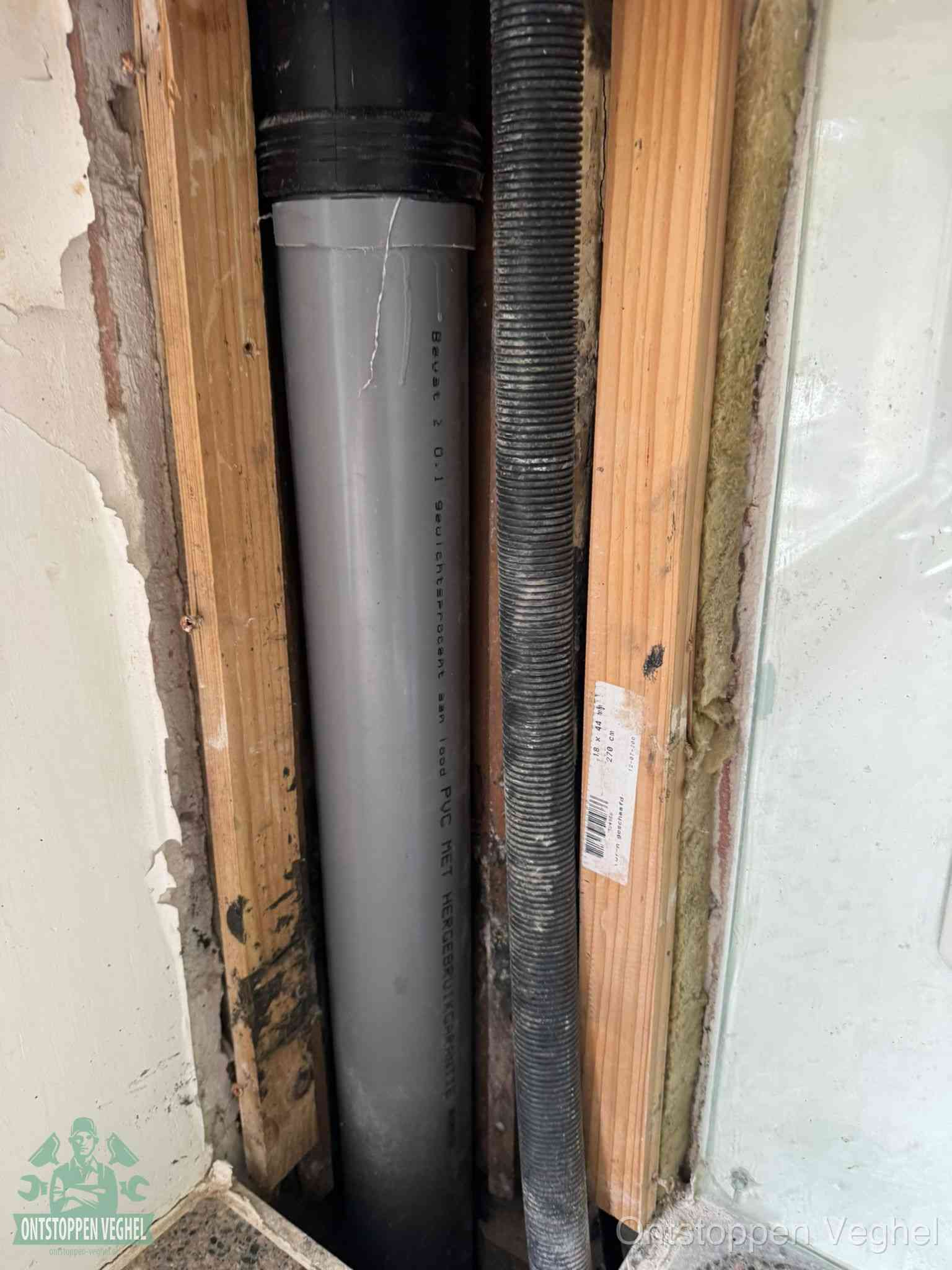 Een grijze PVC-afvoerbuis met een flexibele ribbelslang in een open wandconstructie, een verwaarloosde afvoer die te lang is blijven zitten in Veghel