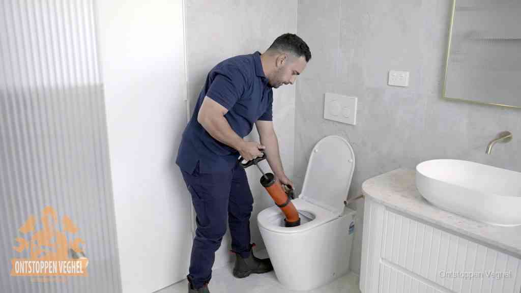 Handmatig de verstopping uit het toilet halen in Veghel Een monteur buigt over een wandcloset en duwt met de hand een persluchtontstopper in de toiletpot om de verstopping handmatig los te maken in Veghel