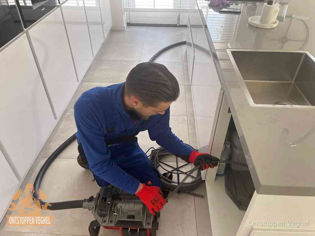 Een monteur ontstopt de keukenafvoer onder de spoelbak met een elektrische veermachine in Veghel