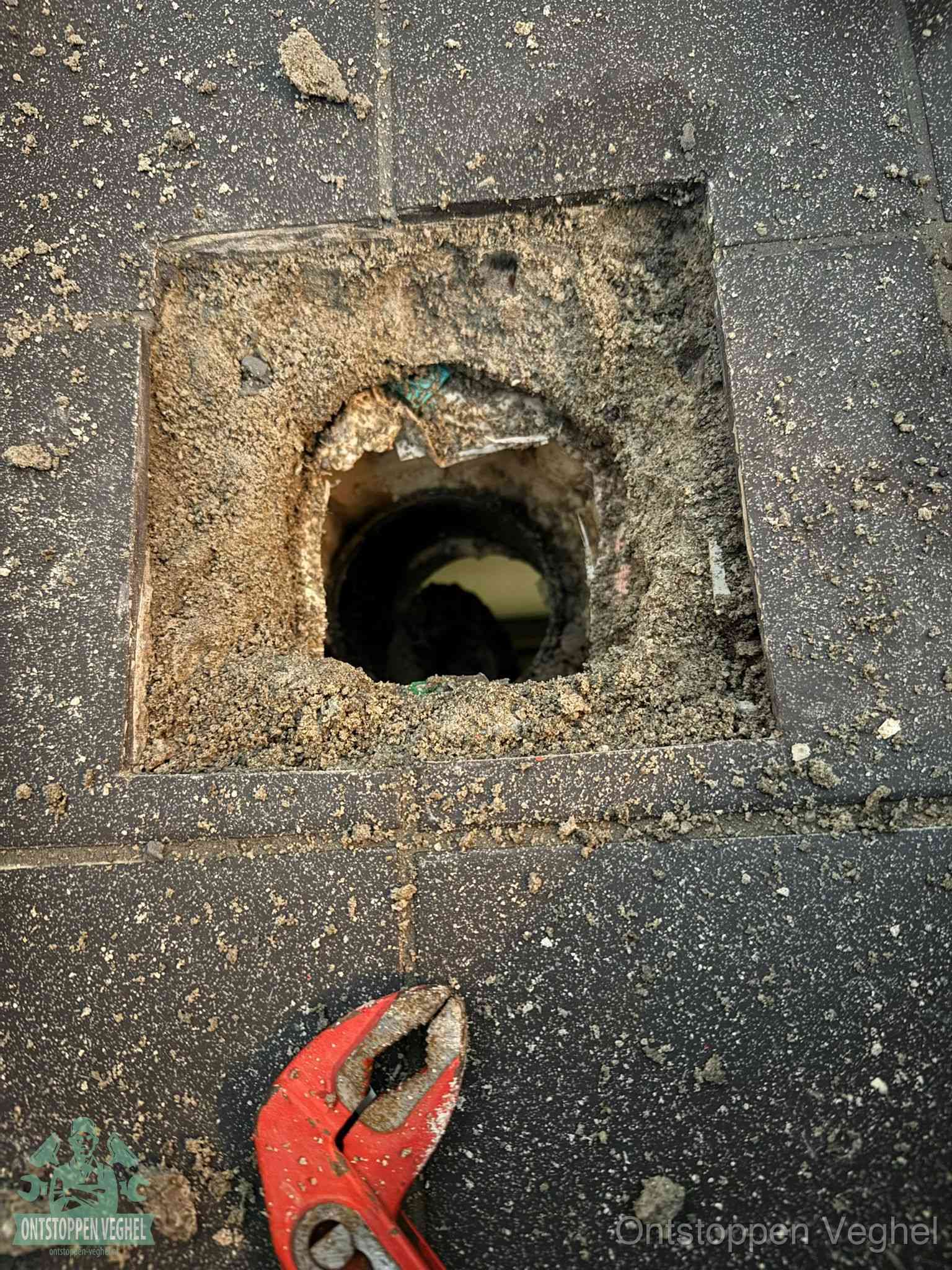 Een geopend rioolputje in een betontegelvloer met losgemaakt rooster en een zichtbare ronde afvoerbuis, het achterhalen waar de afvoerverstopping zit in Veghel