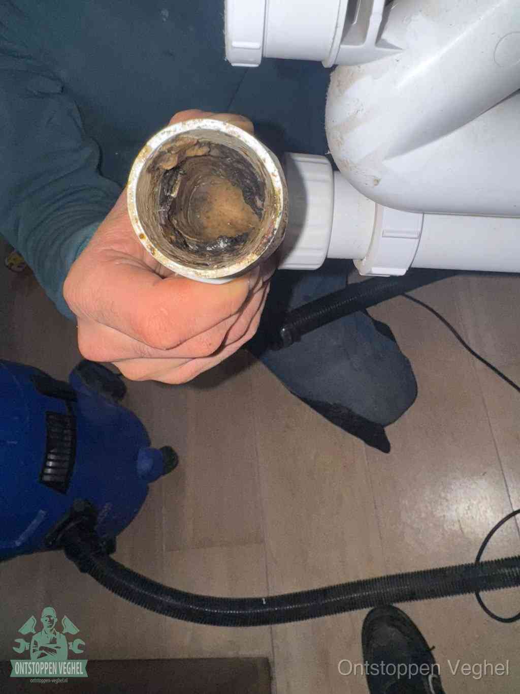Een hand houdt een losgekoppeld PVC-afvoerbuisstuk vast dat van binnen volledig is dichtgeslibd met vet, vuil en aanslag, de meest voorkomende oorzaak van een verstopte afvoer in Veghel