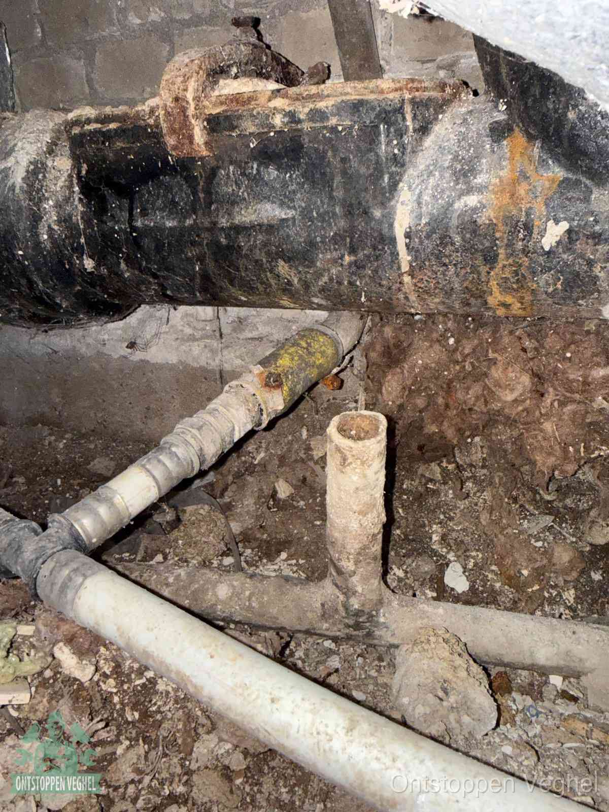 Een dikke zwarte hoofdrioolbuis met roest- en kalkaanslag in een kruipruimte, oorzaak van terugkerende structurele afvoerproblemen in Veghel