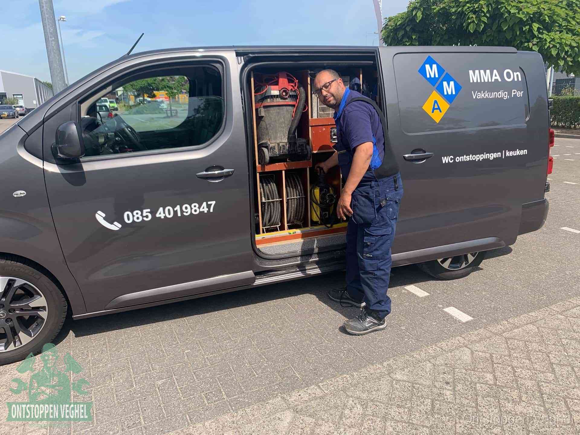 Een monteur bij de open schuifdeur van zijn bedrijfsbus op een parkeerplaats, klaar om de oorzaak van terugkerende afvoerverstoppingen aan te pakken in Veghel