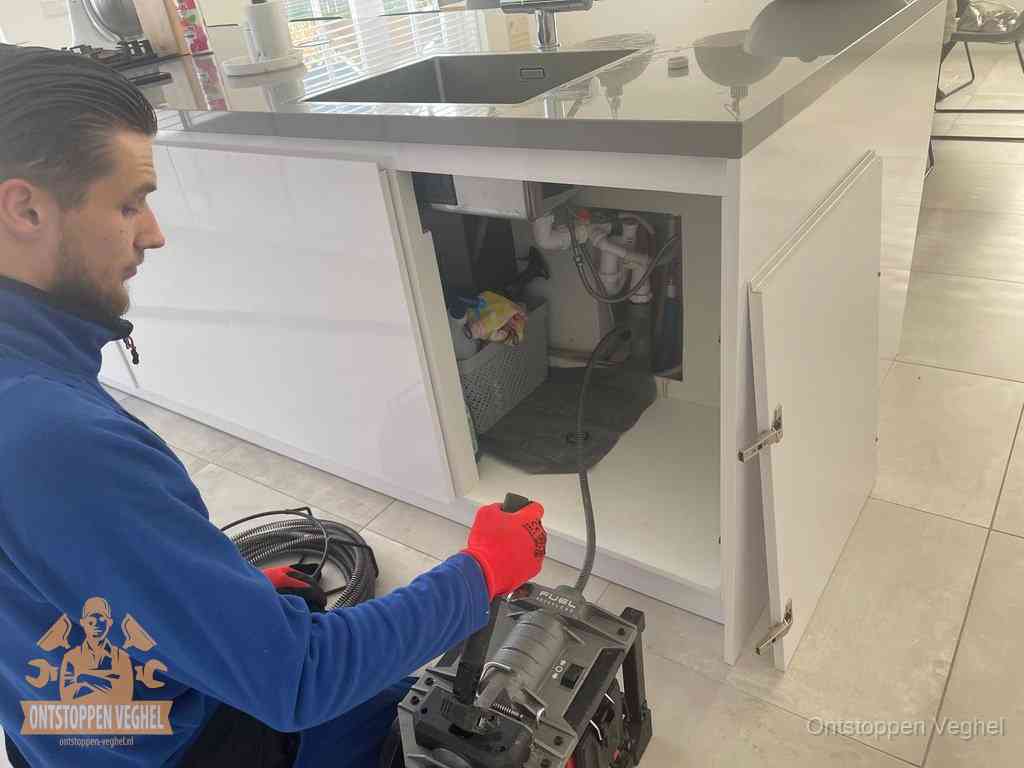 Monteur ontstopt met een veermachine een verstopte afvoer onder de gootsteen in Veghel