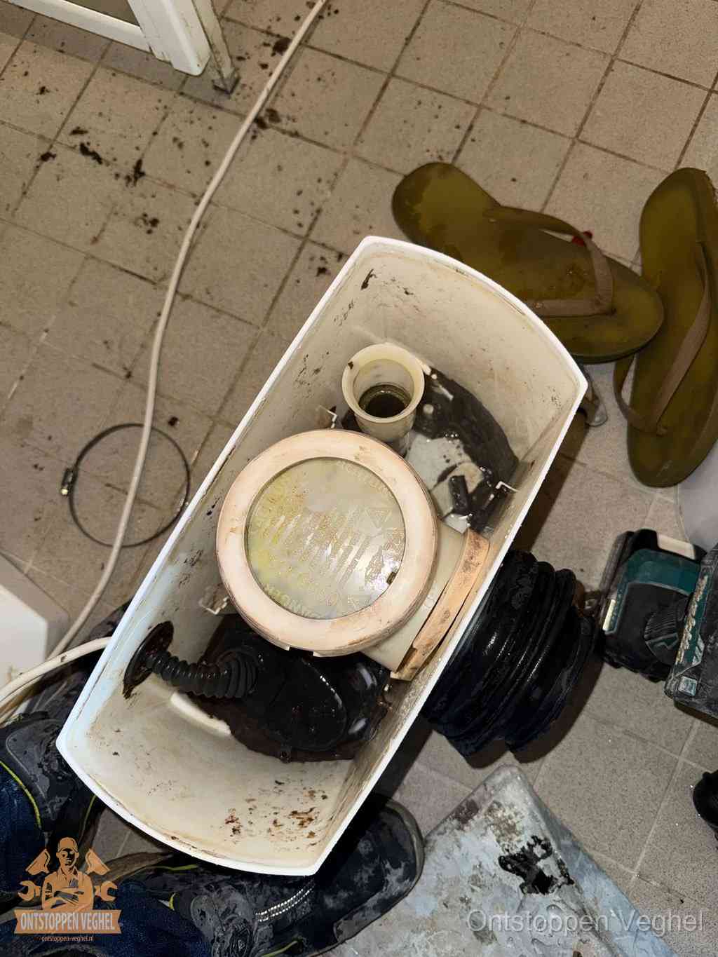 Vreemd voorwerp uit de wc halen in Veghel Een gedemonteerde toiletpot op de vloer met ontstoppingsveer en gereedschap ernaast, het verwijderen van een vastzittend voorwerp uit de wc in Veghel