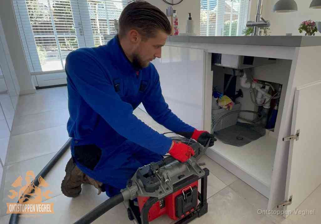 Een monteur voert een professionele elektrische ontstoppingsmachine in de afvoer onder de spoelbak tijdens het gootsteen ontstoppen in Veghel